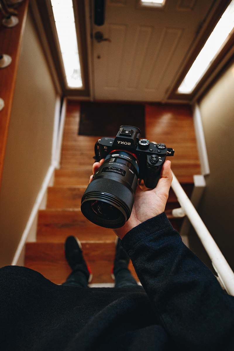 camera person holding black Sony DSLR camera on stair electronics